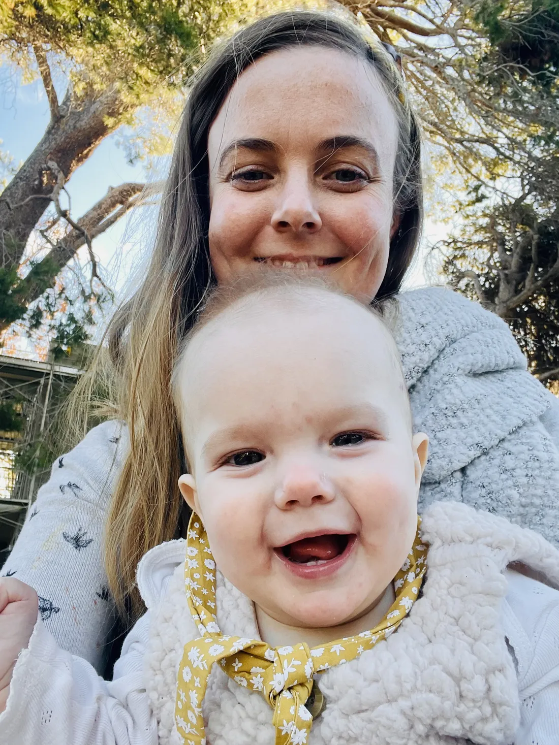 Lily as a baby, smiling, held by her mum outdoors.