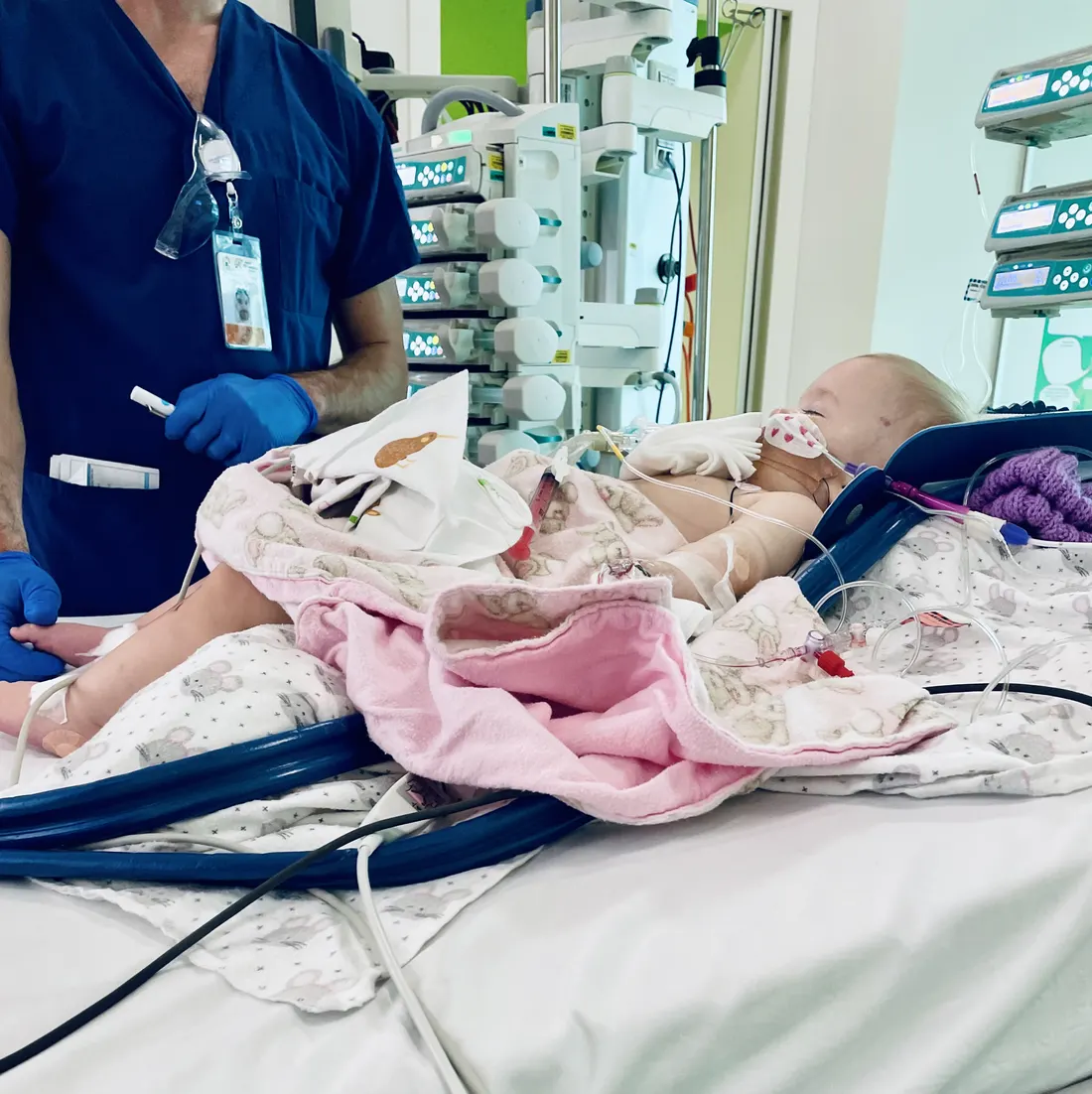 Lily in a hospital intensive care bed, wrapped in a pink blanket, a nurse beside her.